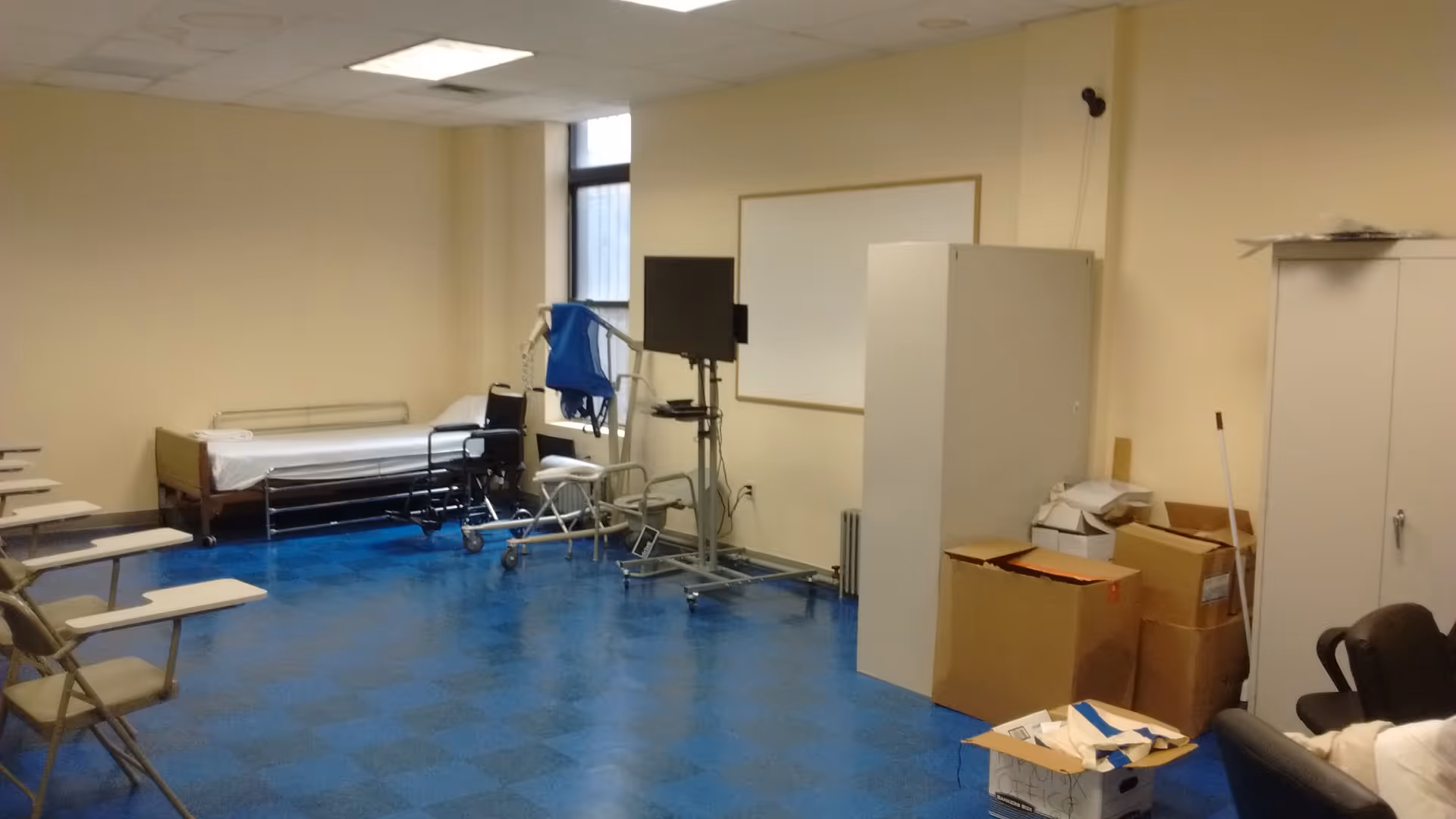 Interior care room with a bed, medical equipment, and scattered boxes.
