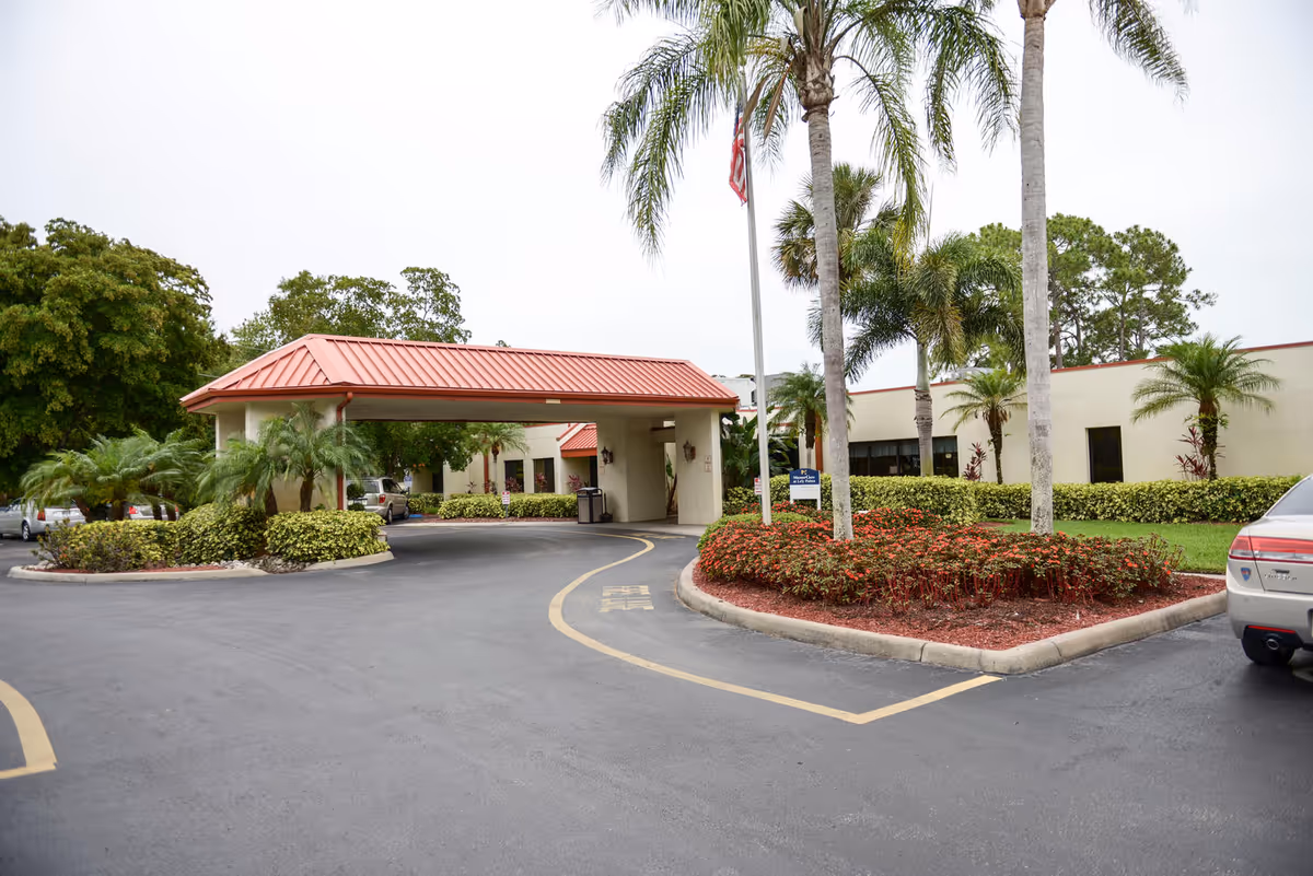 Paved driveway curves toward Solaris Healthcare Lely Palms entrance beneath a red-tiled canopy