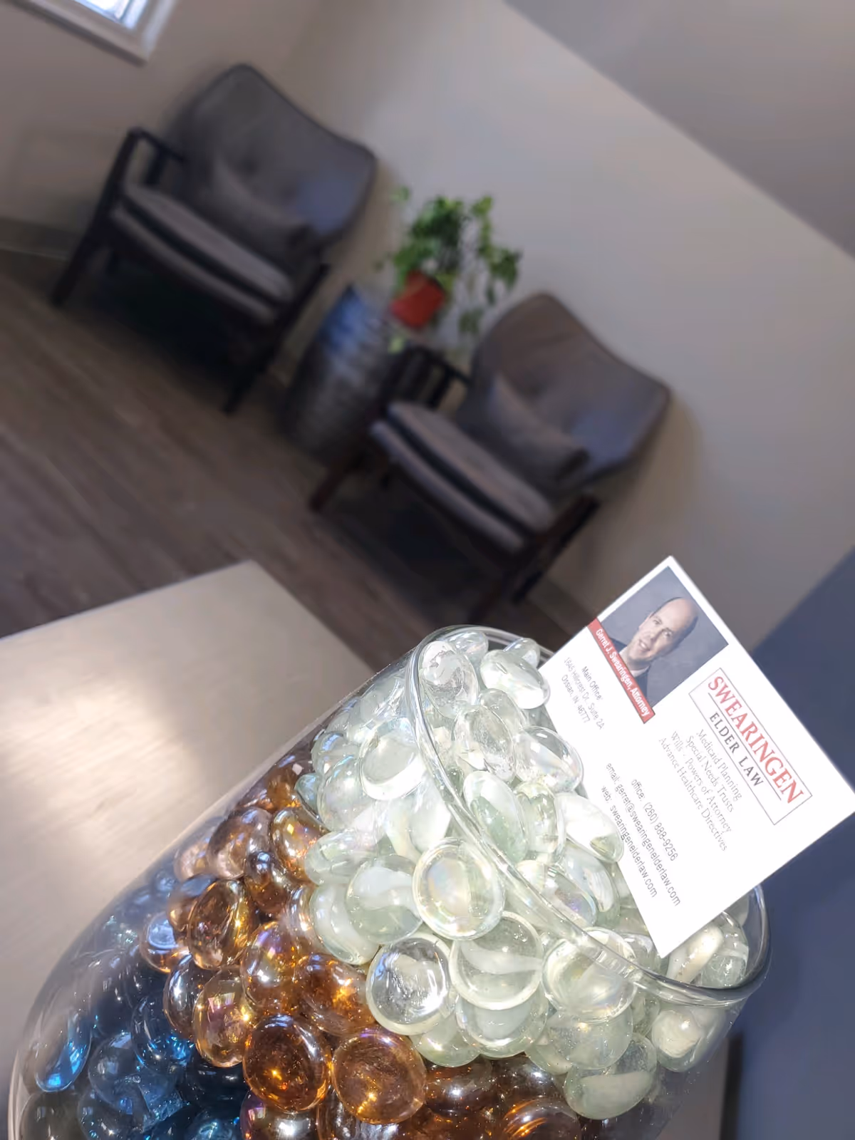 Glass pebbles fill a bowl on a table in a waiting area with chairs and plant