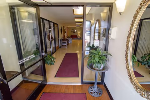 Hotel-like lobby entrance with glass doors, maroon runners, plants, and a round mirror.