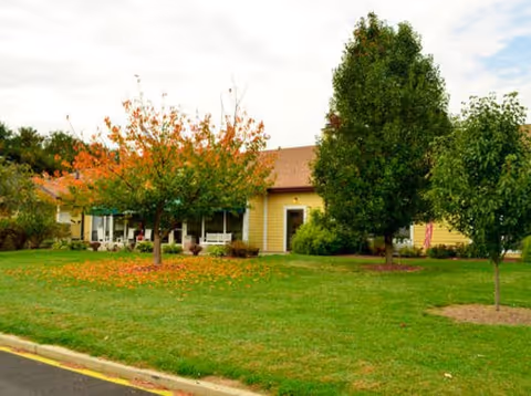 Single-story yellow Brookdale Dover building with lawn and trees in front
