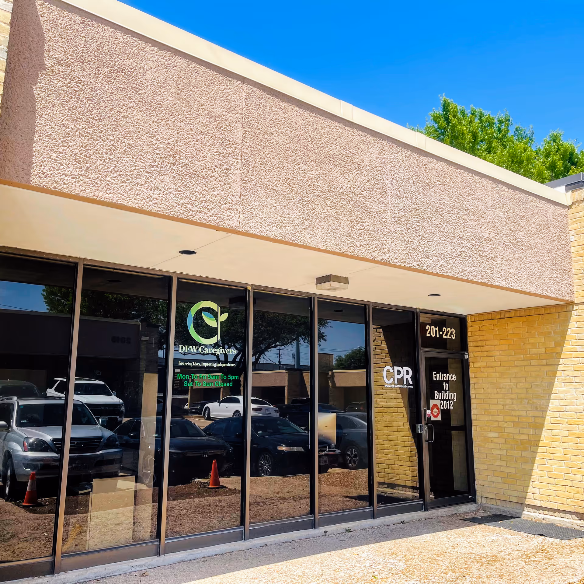 Exterior view of a DFW Caregivers storefront with glass doors, logo, and reflected cars.
