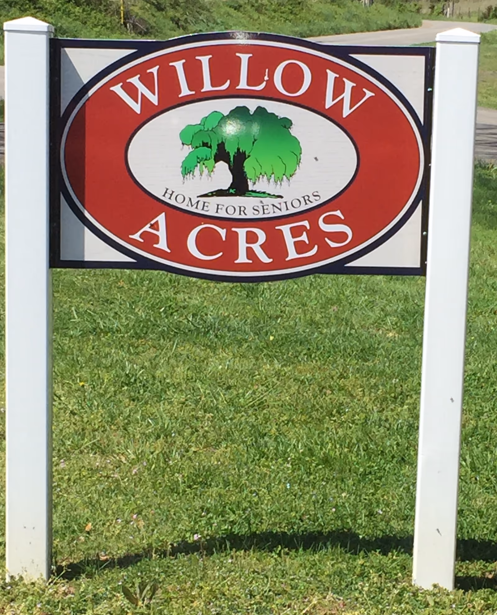Outdoor Willow Acres sign with green tree graphic, mounted between white posts on a grassy lawn.