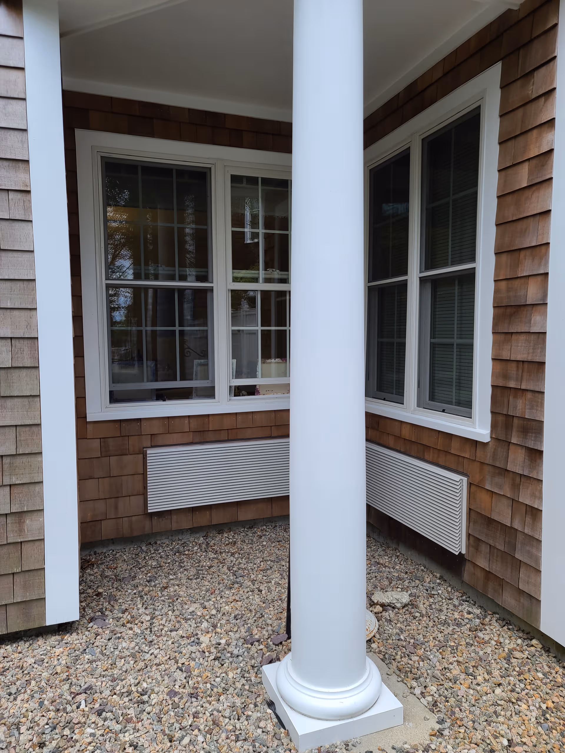 Exterior corner of a senior living building with a white column and gravel ground.