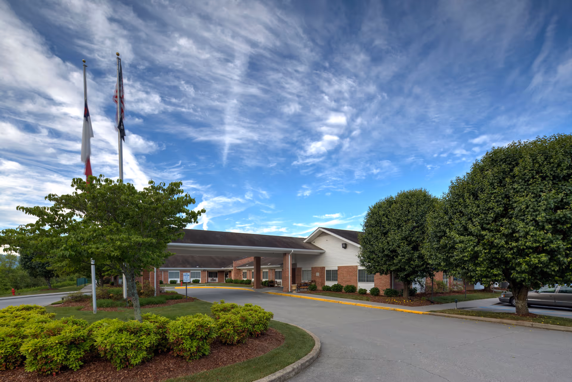 Exterior view of Lakebridge - A Waters Community with flags, trees, and a curved driveway.