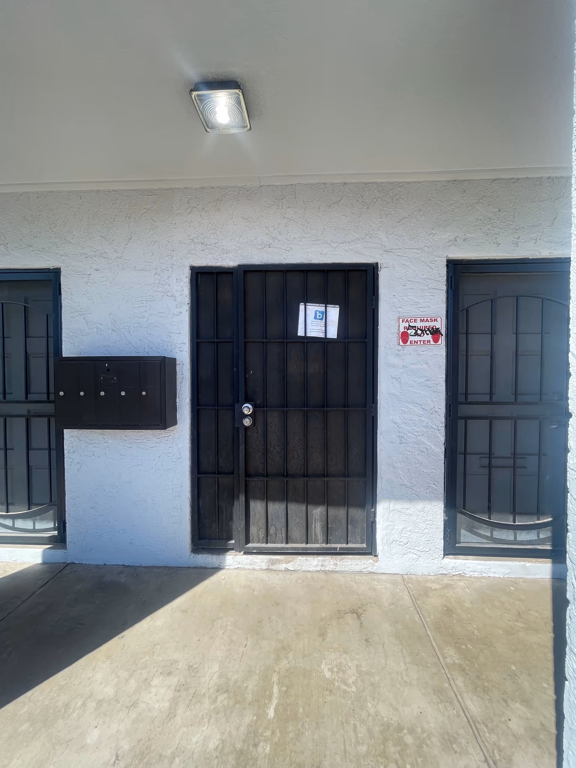 Exterior facility entrance with black metal doors, mailbox, and a face mask sign.