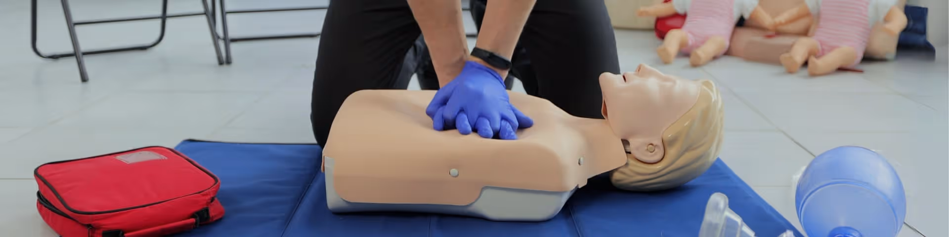 Person wearing gloves performs CPR on a lifelike mannequin on a blue mat indoors.