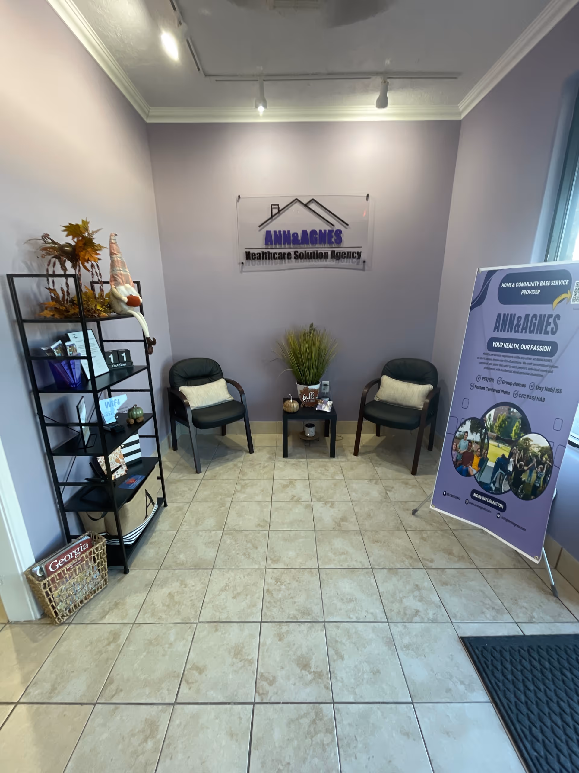 A small reception lobby with two chairs, plants, shelves, and a promotional banner.
