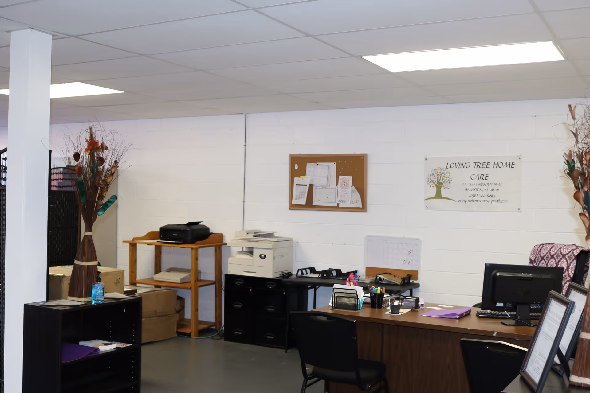 Interior office of Loving Tree Home Care with desk, printer, corkboard, and sign.