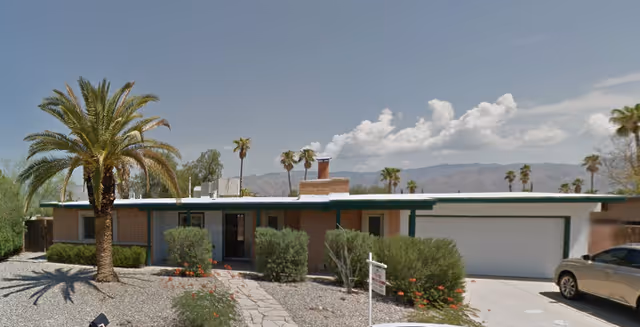 Single-story care home exterior with palm trees, desert landscaping, and a two-car garage