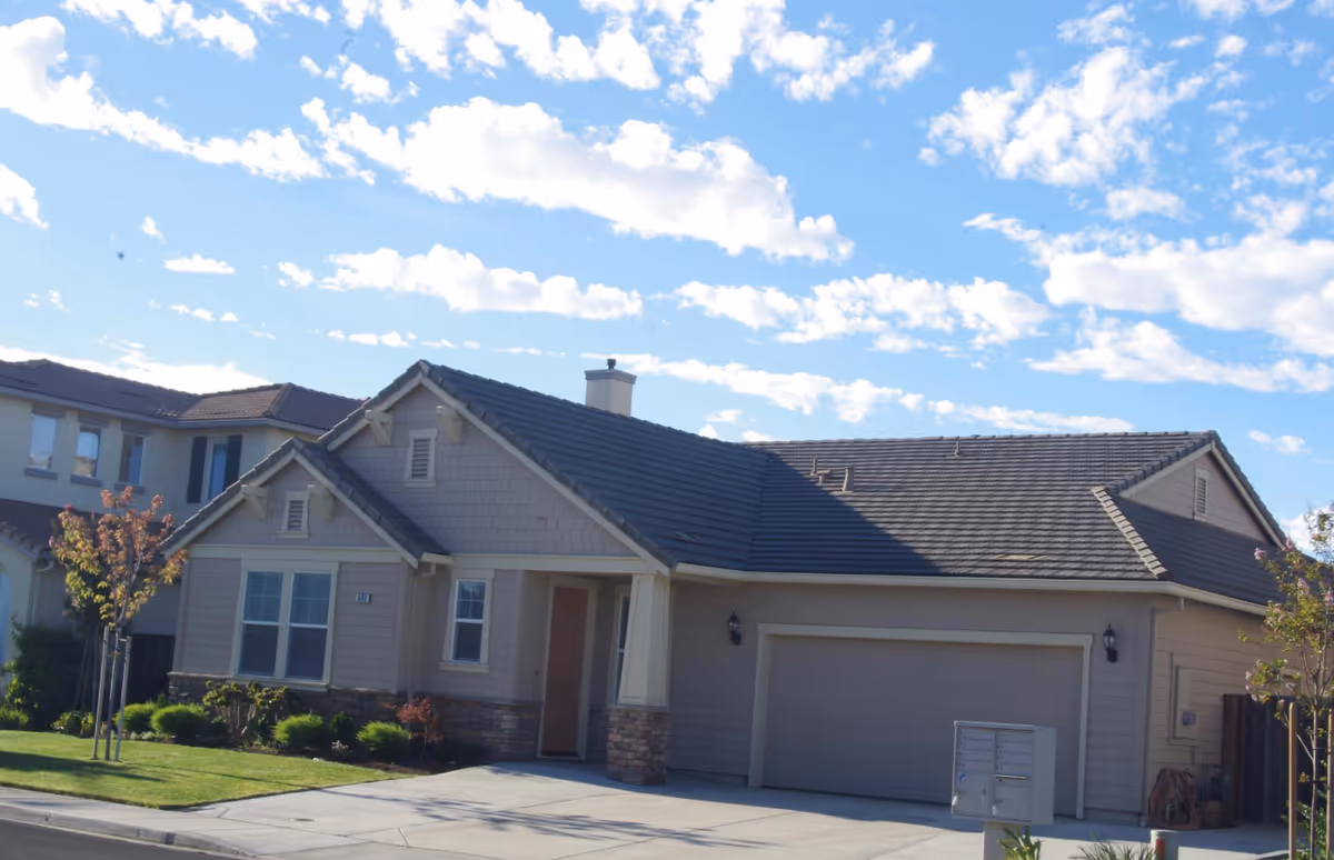 Modern senior living facility exterior with beige siding, a two-car garage, and a manicured lawn.