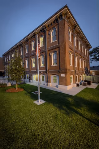 Exterior brick senior living building with flagpole on a green lawn.
