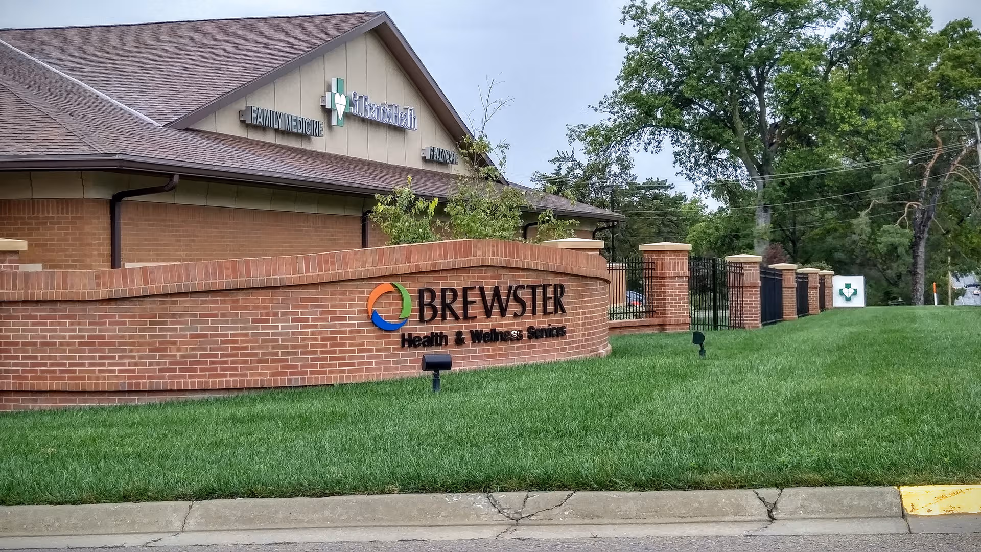 Exterior view of Brewster facility with brick sign wall, green lawn, and building facade.