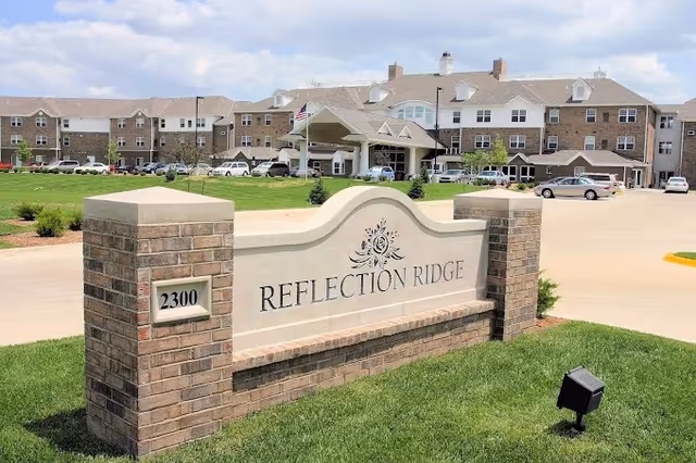 Entrance sign for Reflection Ridge senior living, with brick pillars and a curved stone plaque.