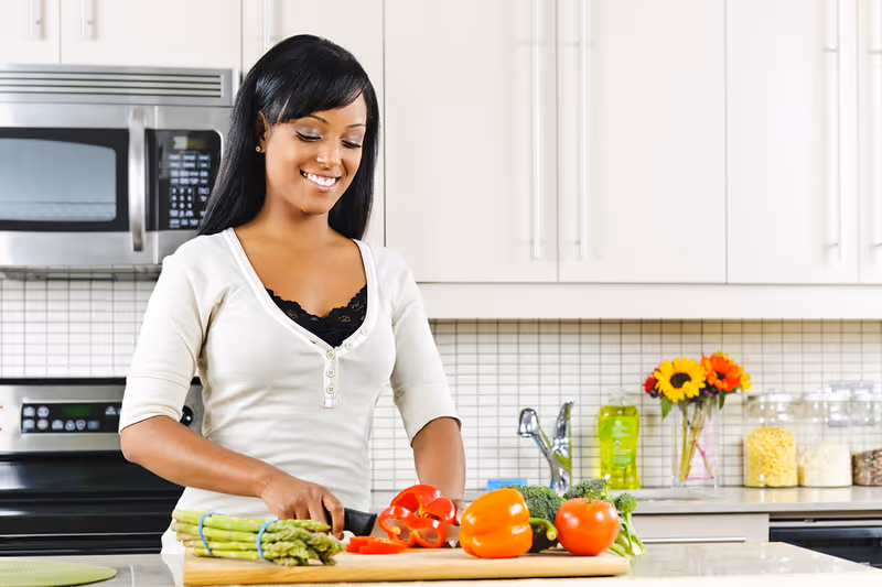 Smiling woman chops vegetables on a cutting board in a bright, modern kitchen.