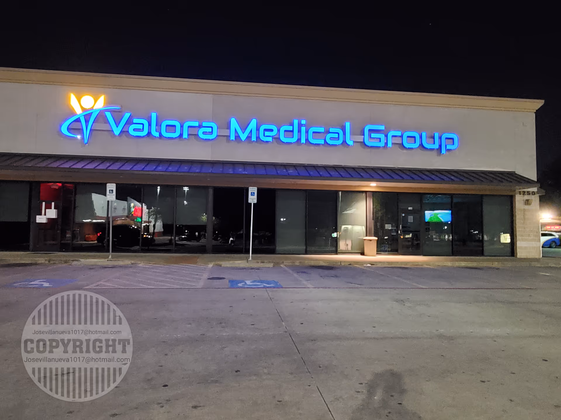 Night exterior of Valora Medical Group Arlington storefront with blue sign and parking lot.