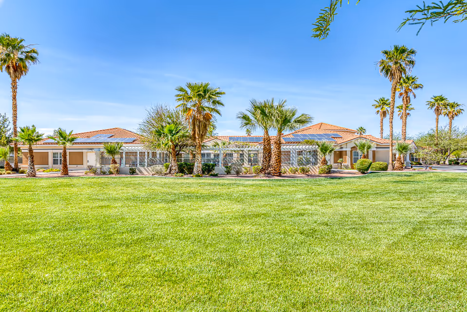 Front view of a single-story Spring Valley Memory Care building with palm trees and a large green lawn under a blue sky.