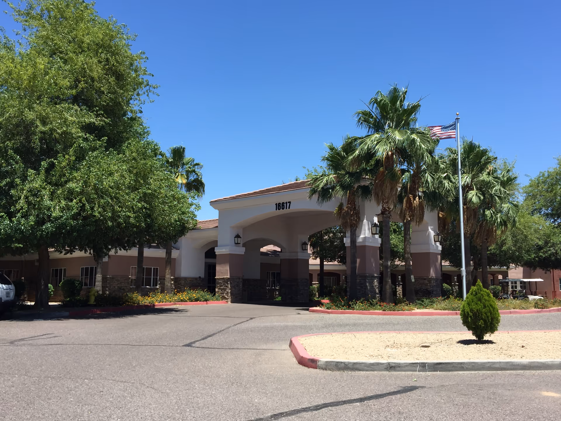 Assisted living facility entrance with palm trees and a porte-cochère under a blue sky.