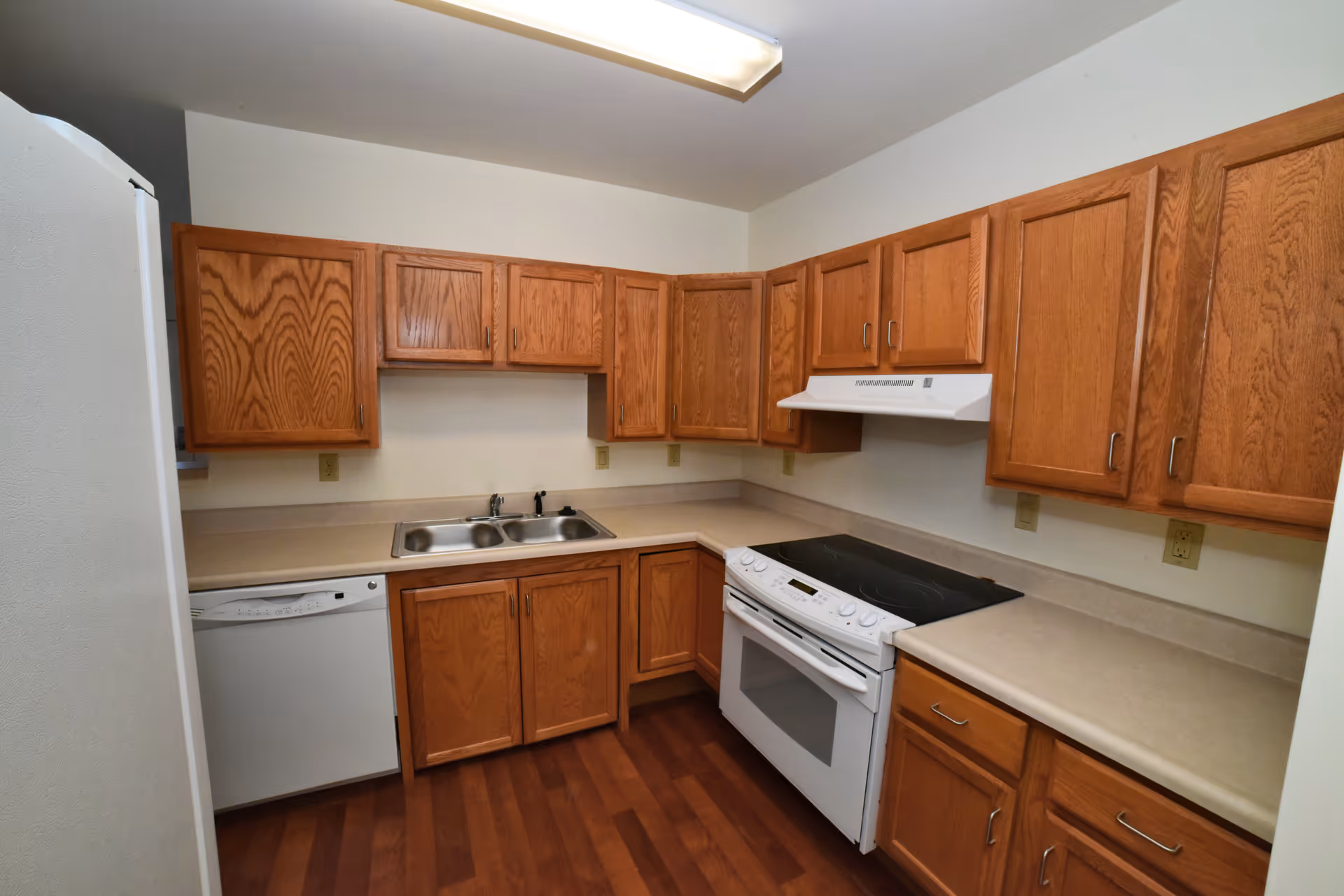 U-shaped kitchen in a senior living facility with wooden cabinets, sink, stove, and dishwasher.