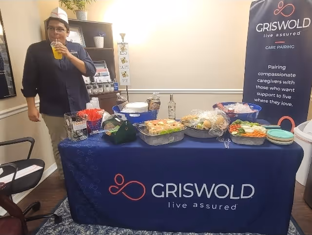 Staff member in uniform stands beside a snack table at a Griswold care event.
