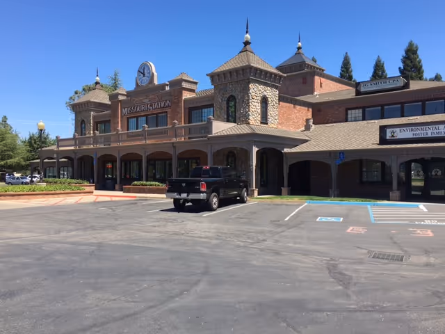 Exterior view of a brick senior living facility with arched entrance and parking.