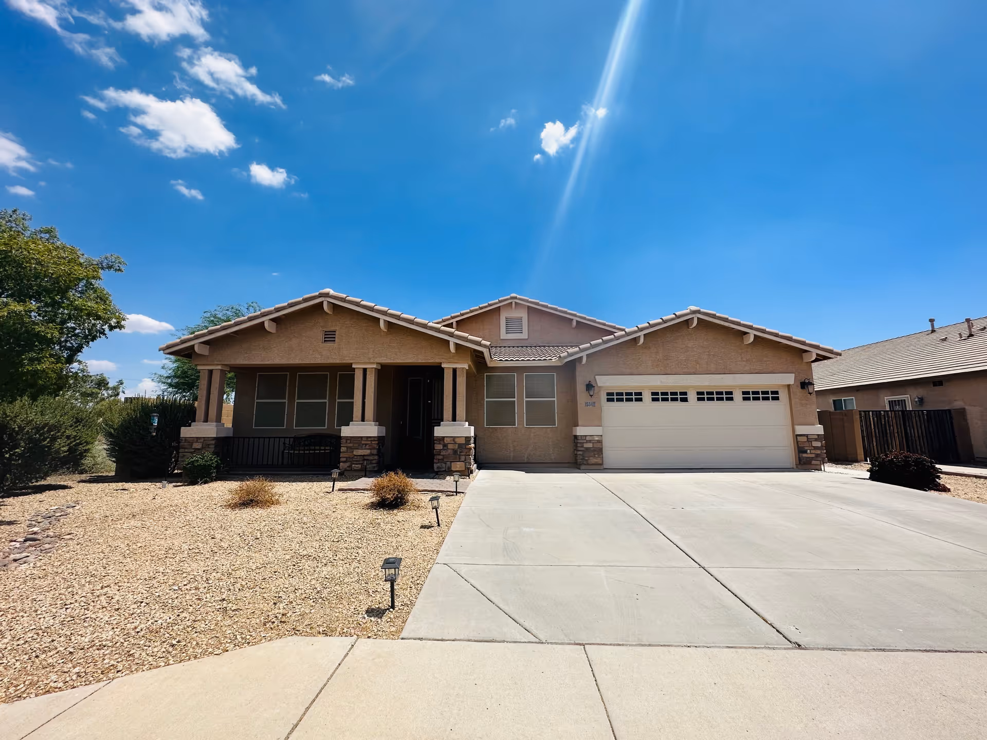 Front exterior of a beige, single-story house with a two-car garage and desert yard.