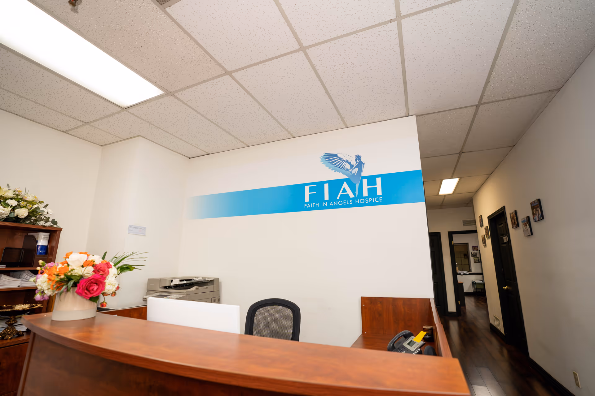 Reception desk with flowers and a blue Faith In Angels Hospice sign on wall.