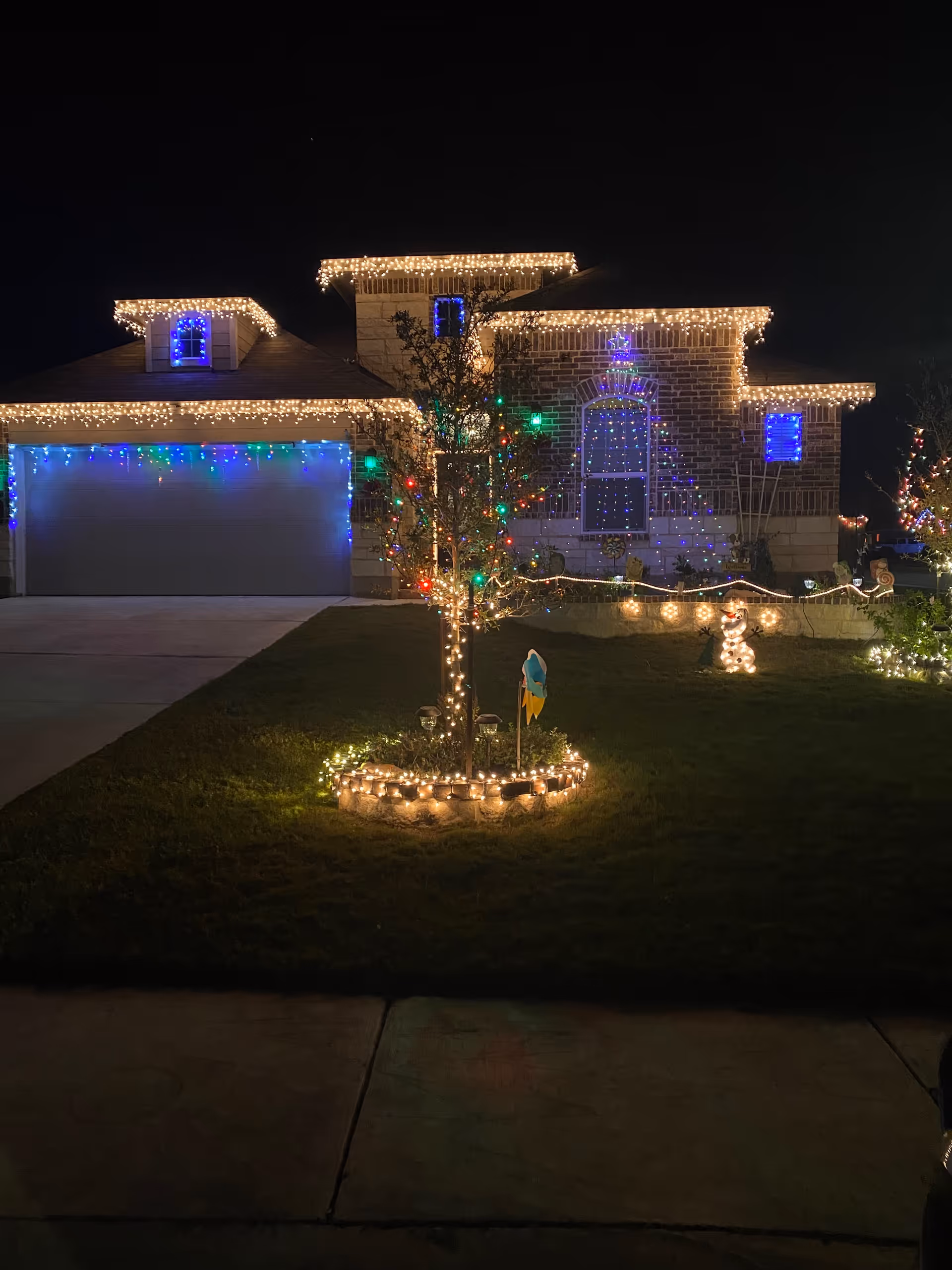 Front exterior of a brick home illuminated with Christmas lights and a lit tree.
