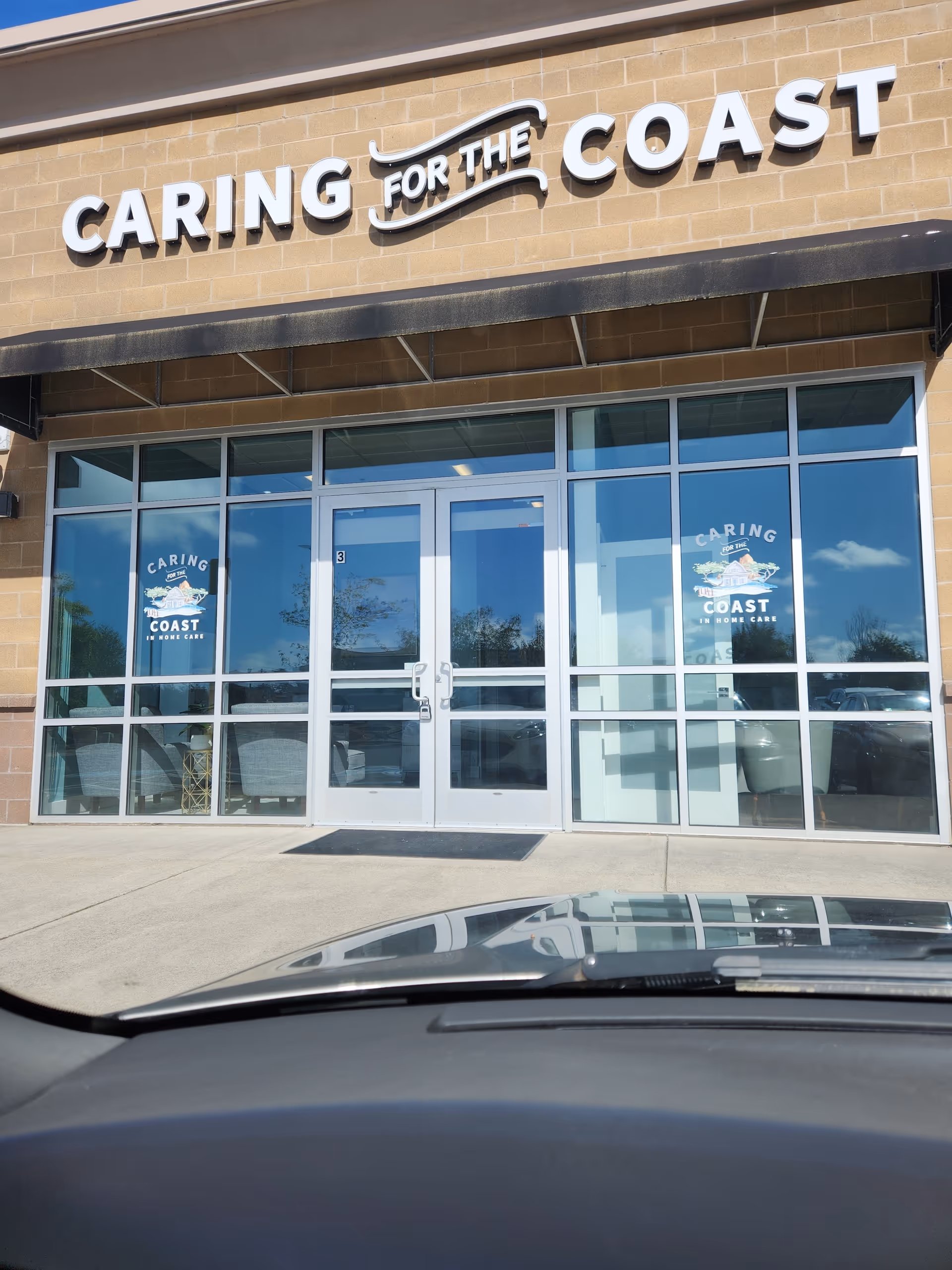 Exterior view of Caring for the Coast facility with glass entry doors and sign.