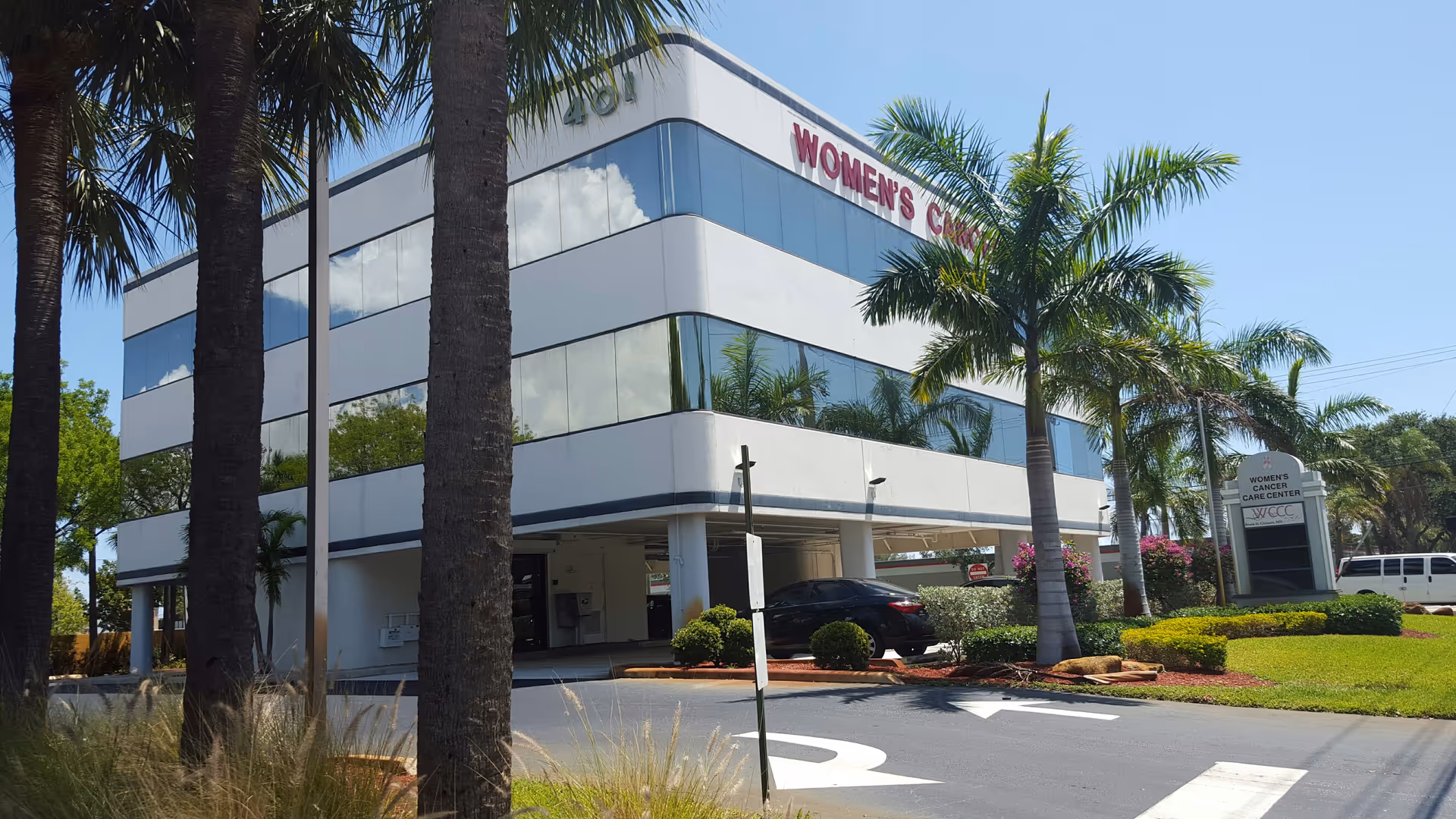 Modern two-story building with glass windows and palm trees near the entrance.