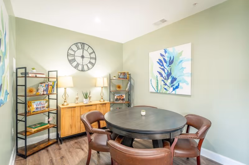 Cozy indoor dining area with round table, chairs, bookshelves, and wall art.
