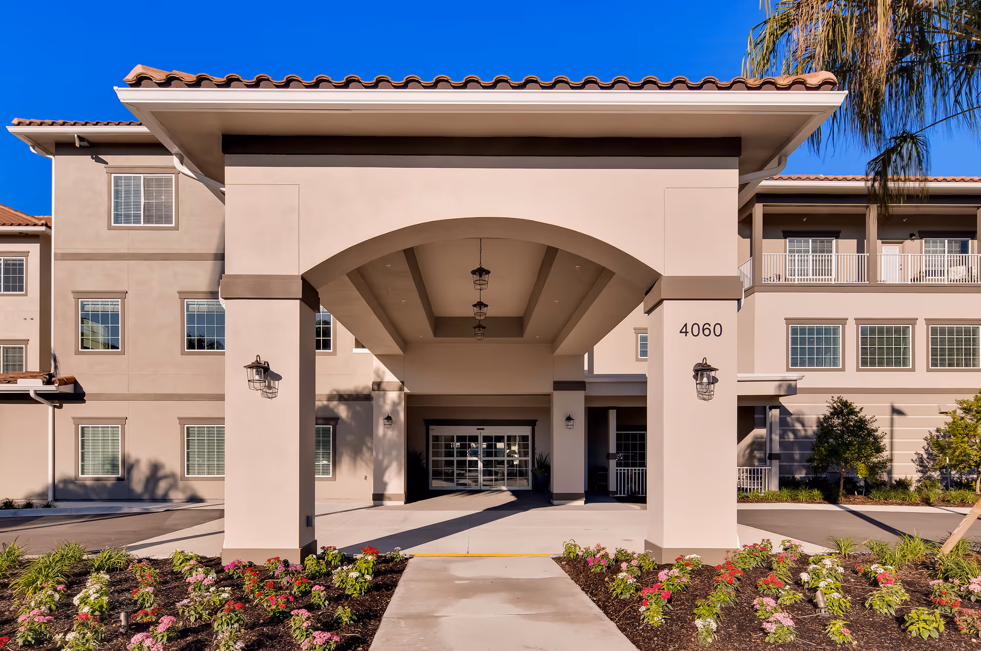 Front entrance of a senior living building with a covered porte-cochere, address number 4060, and landscaped flowerbeds.