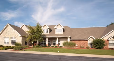 One-story brick-and-stone residential building with gabled roof, dormer windows, front lawn and driveway under a blue sky.