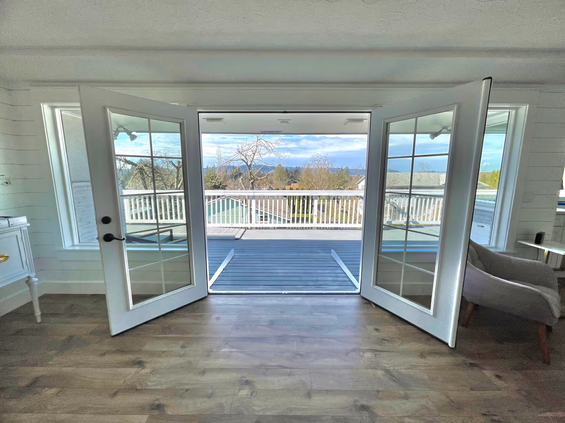 Open French doors in a living room leading out to a balcony with a view of trees and rooftops.