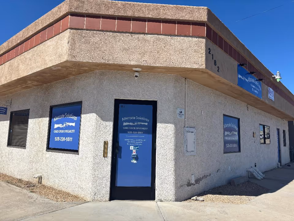 Exterior view of a beige building with blue signs for Alternate Solutions Care Giver Specialist.