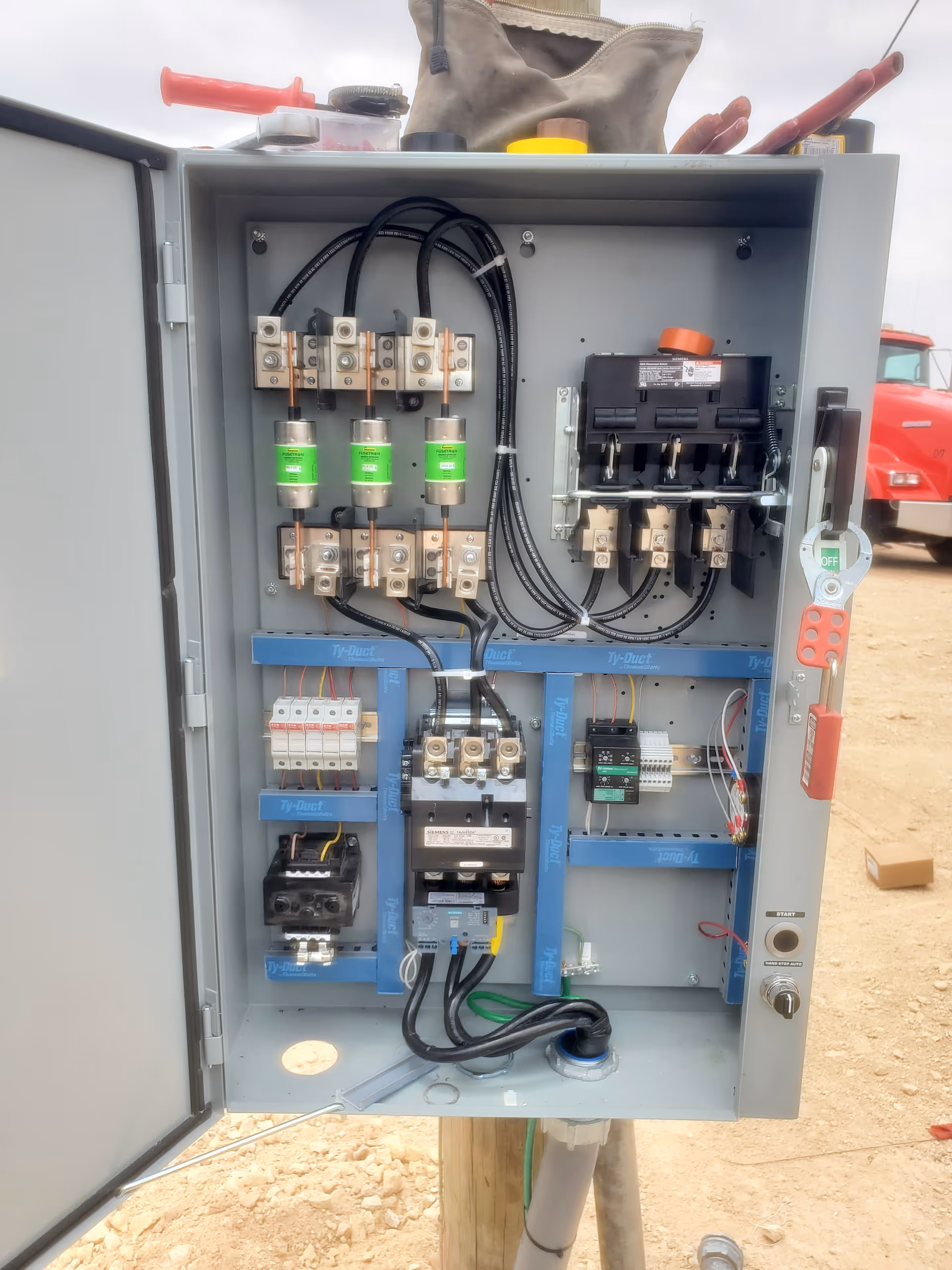 Open electrical control panel with wires and breakers outdoors.