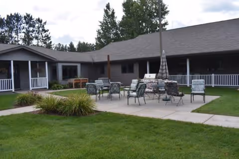 Outdoor patio area with chairs, tables, and an umbrella in front of a single-story facility building.