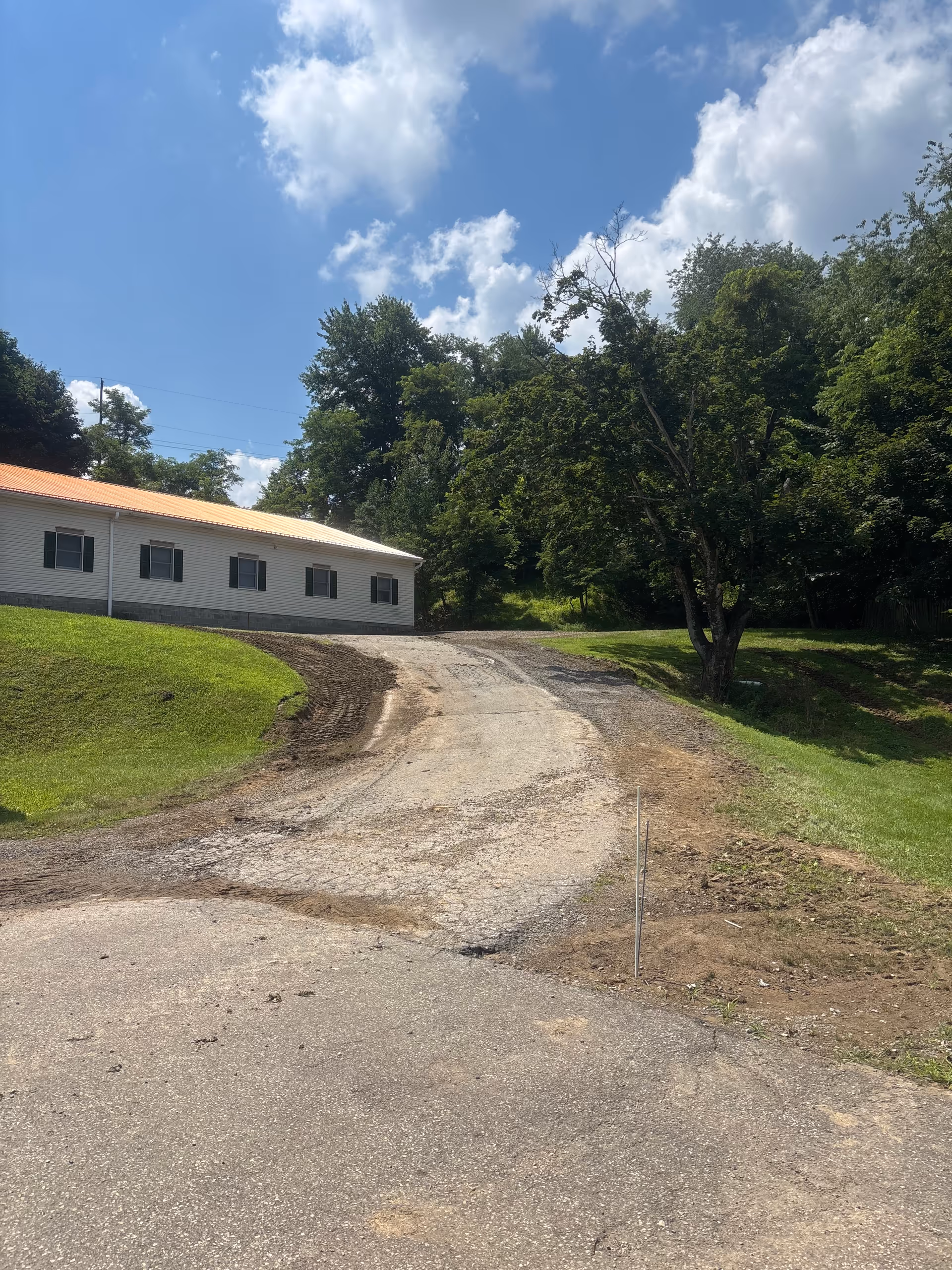 Gravel driveway curves toward a single-story facility with orange roof and surrounding trees.