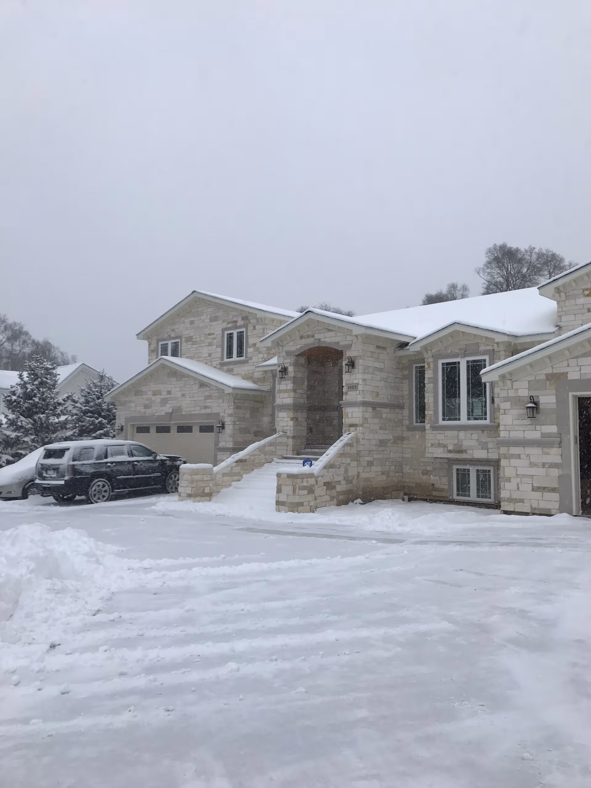 Snow-covered stone building exterior with steps to the front entrance and parked cars.