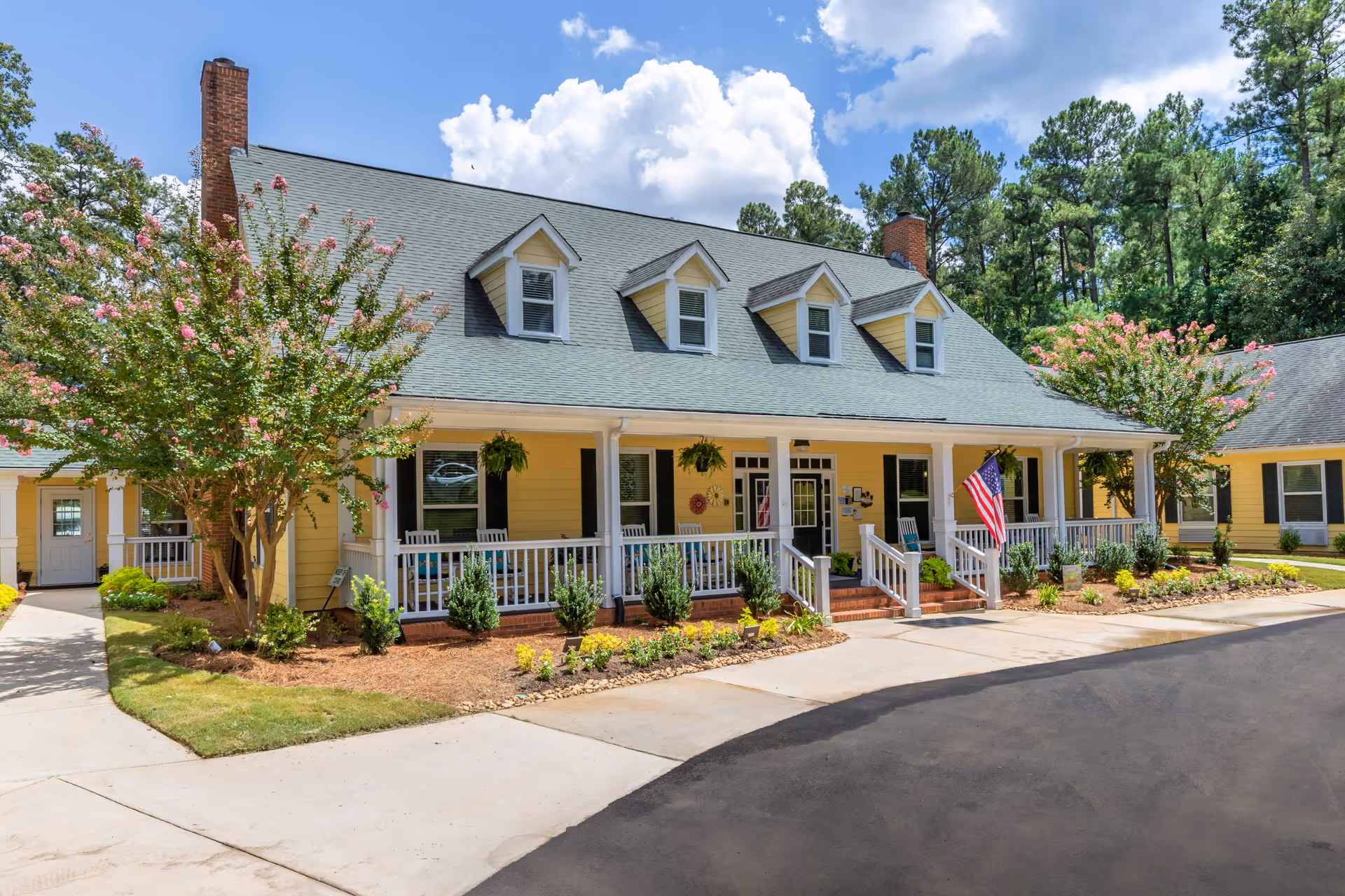 Yellow senior living facility with a covered front porch, landscaping, and trees.