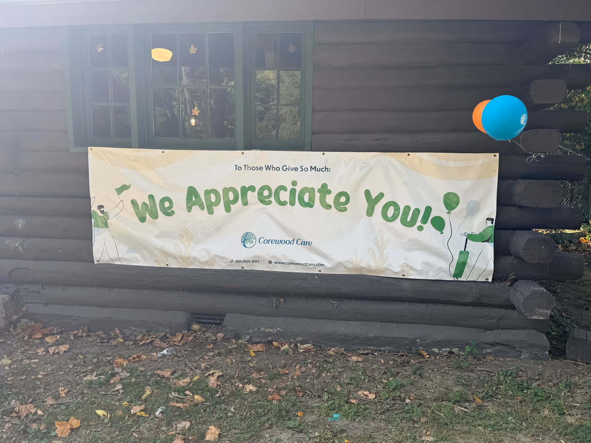A log cabin exterior with a banner reading We Appreciate You and balloons.