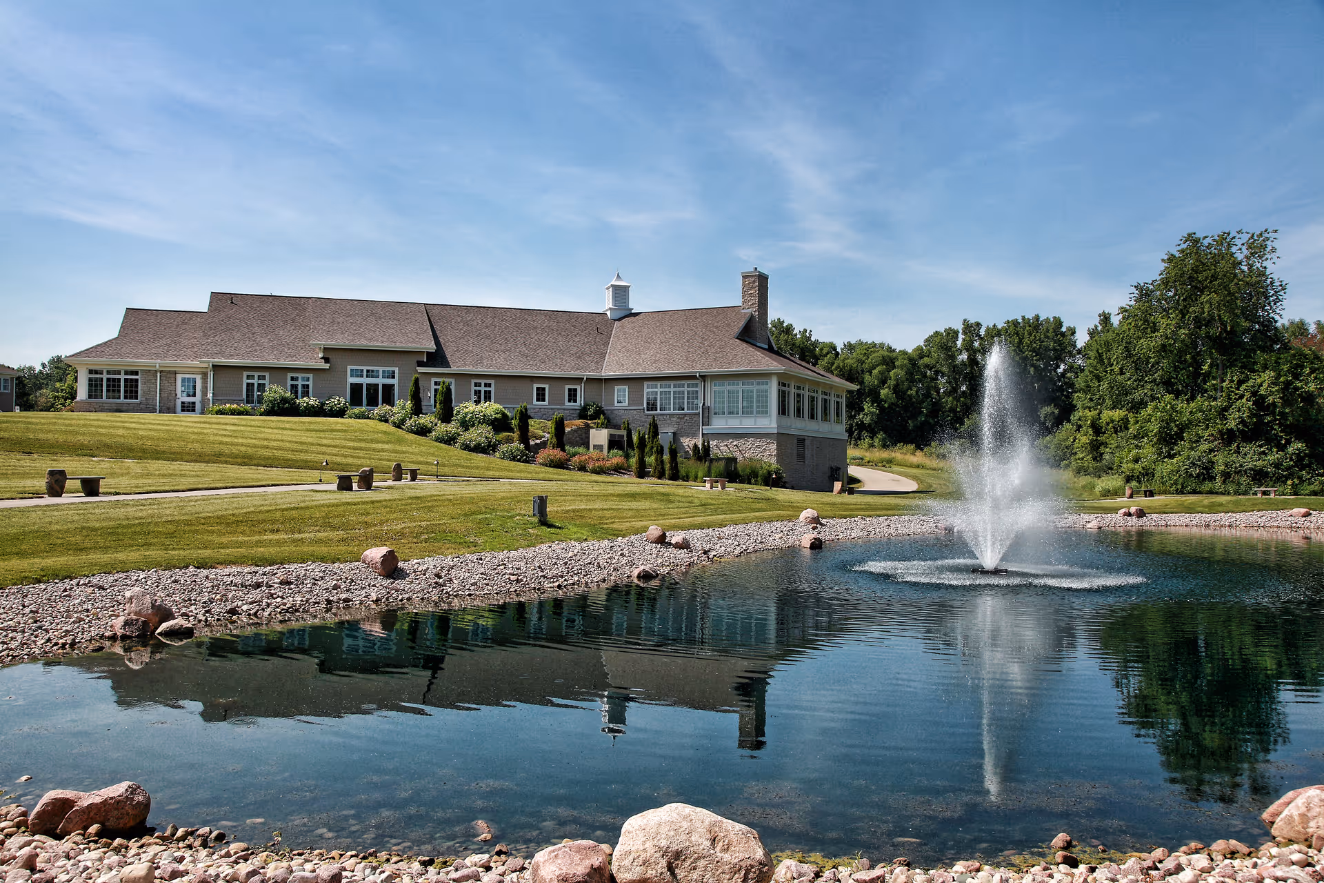 Exterior view of a single-story facility with a manicured lawn and fountain pond.