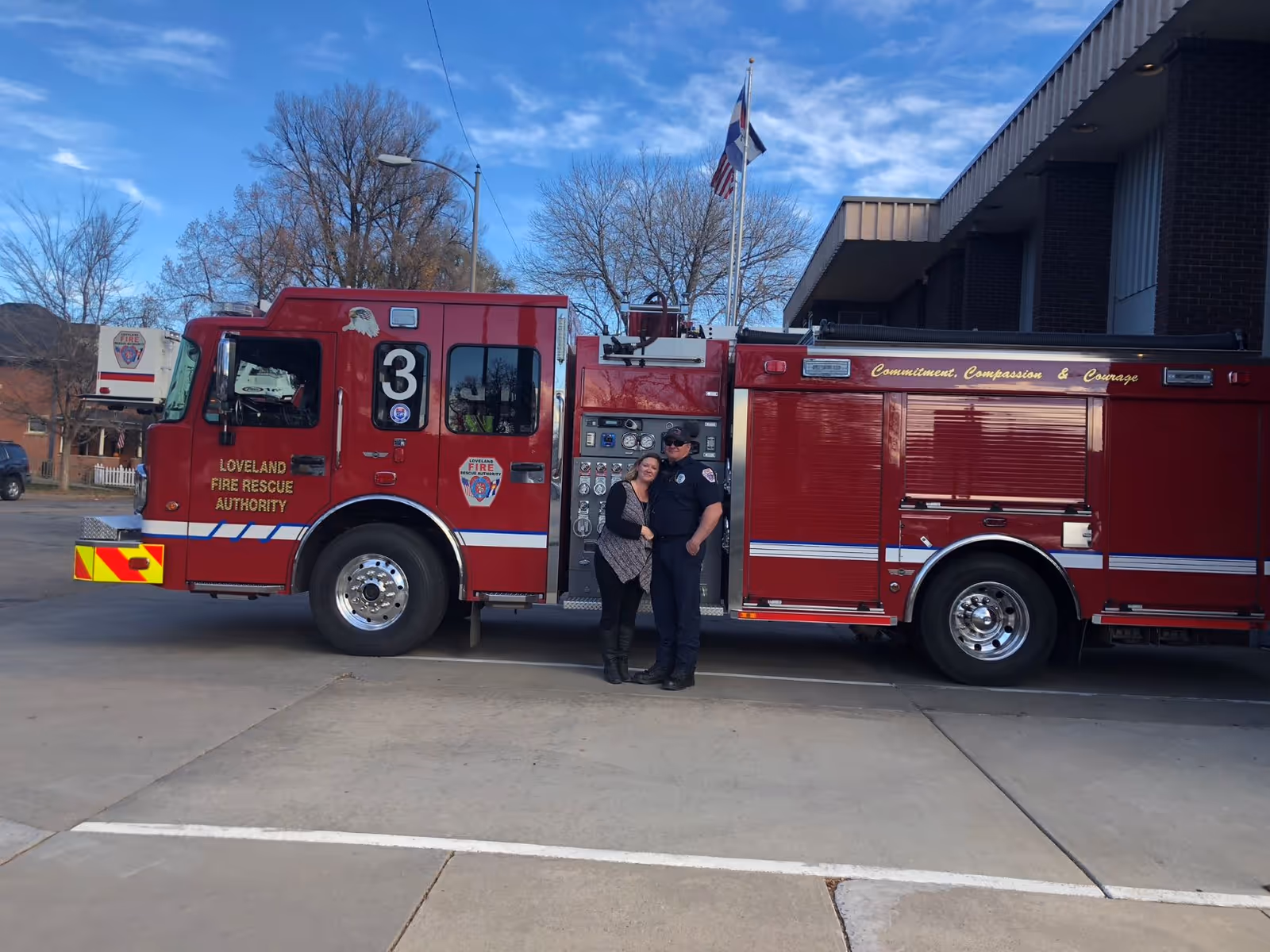 Two people stand beside a red fire truck parked outside a building.