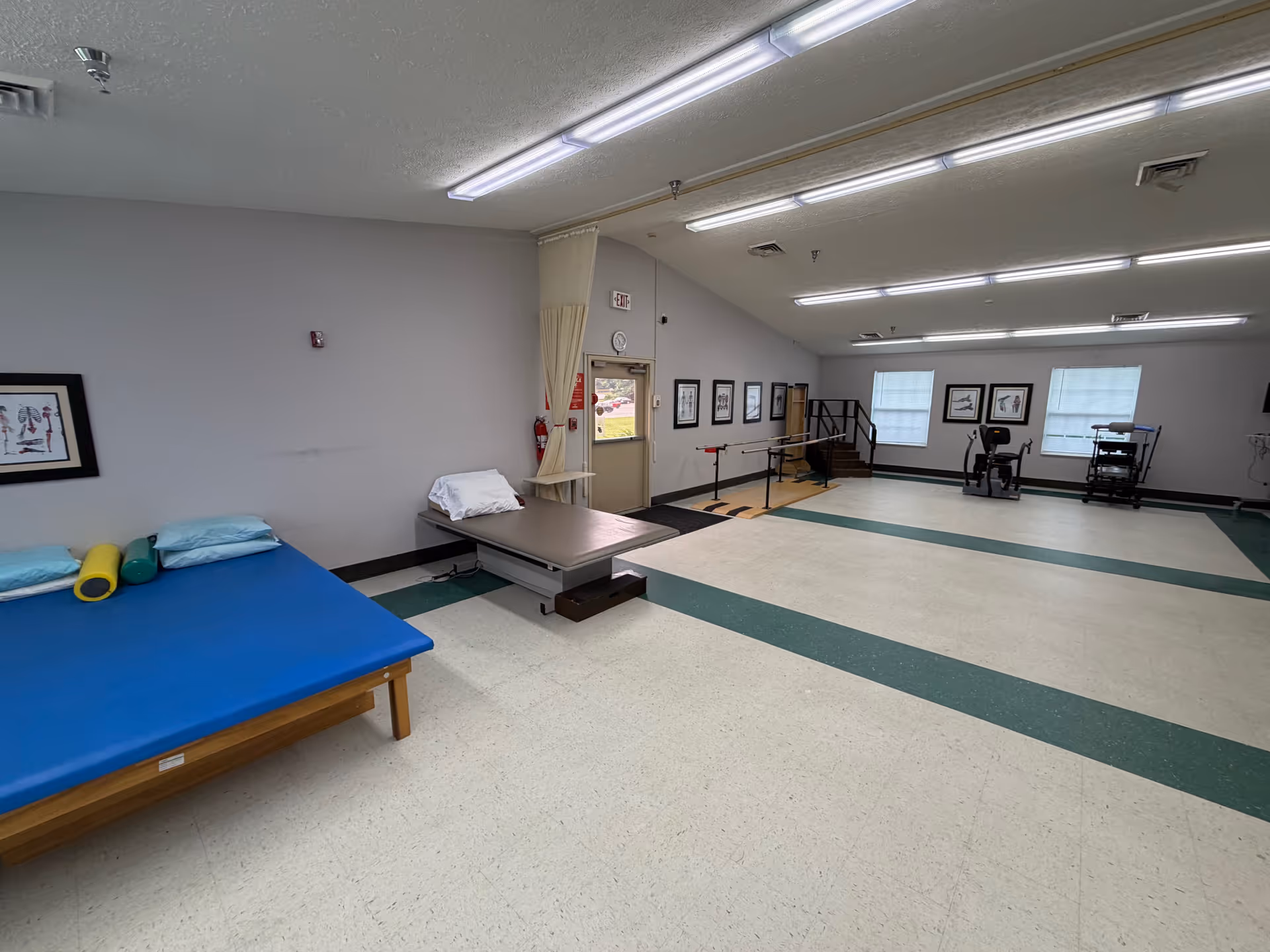 Empty therapy gym with mats, parallel bars, and exercise machines in a senior care center.