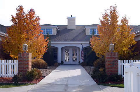 Front entrance of Credo Senior Living with autumn trees and white picket fencing.