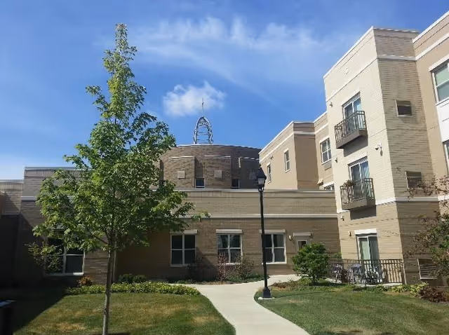 Exterior view of Mercy Circle senior living building with sidewalk, lawn, trees, and streetlamp.