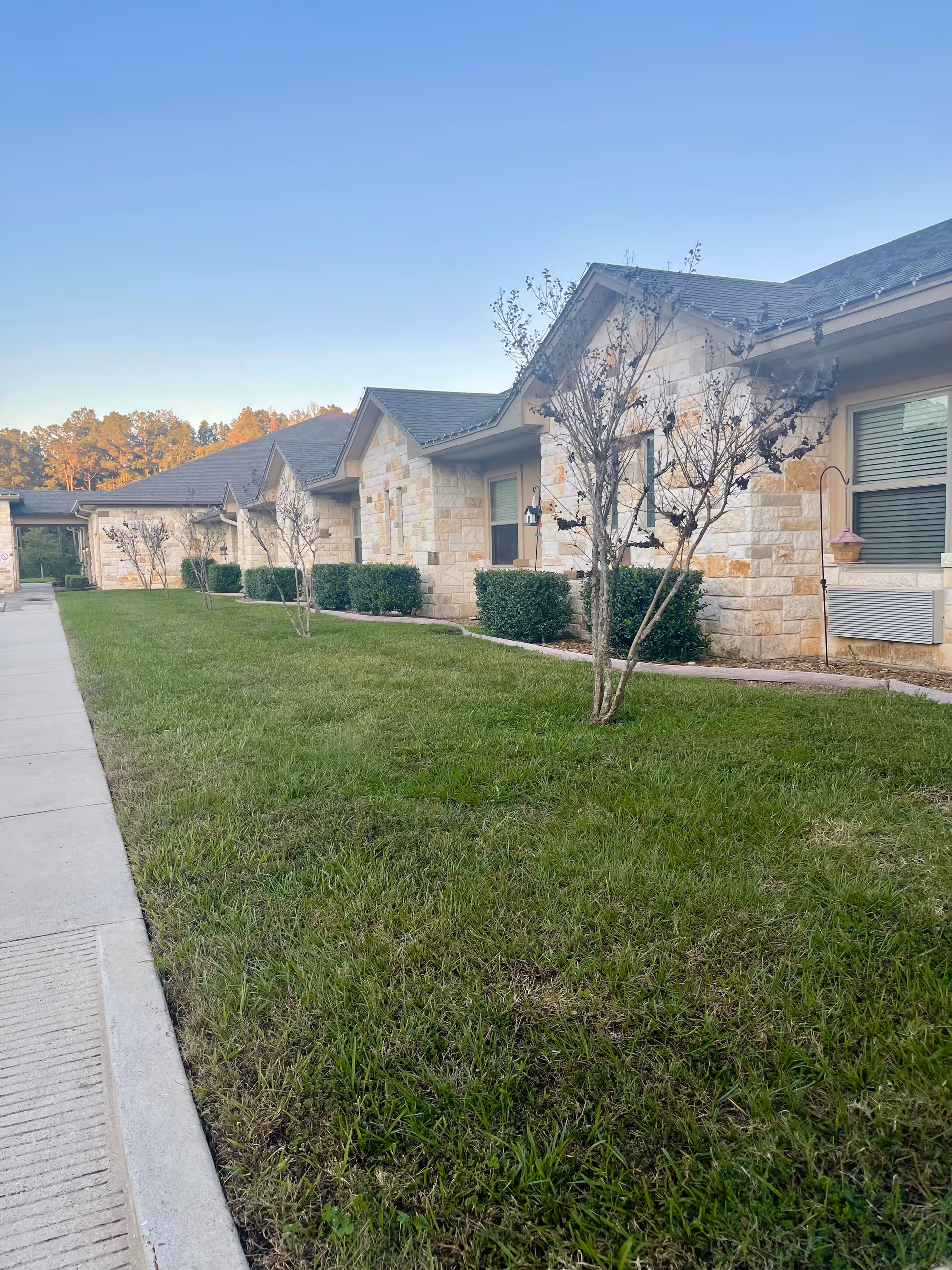 Exterior view of a stone senior living facility with a manicured lawn and trees.