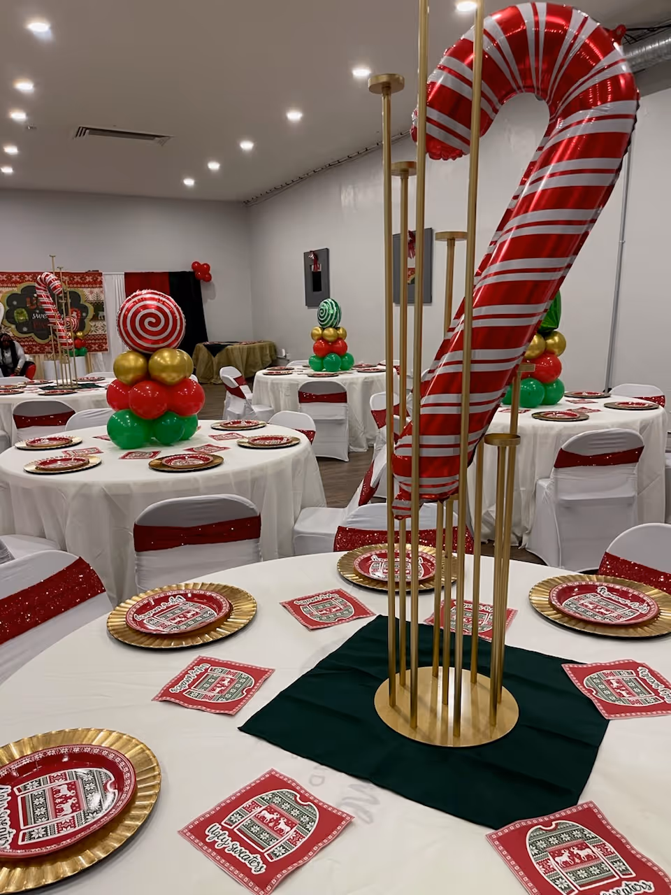 Decorated banquet hall with round tables, white cloths, and candy cane centerpiece.