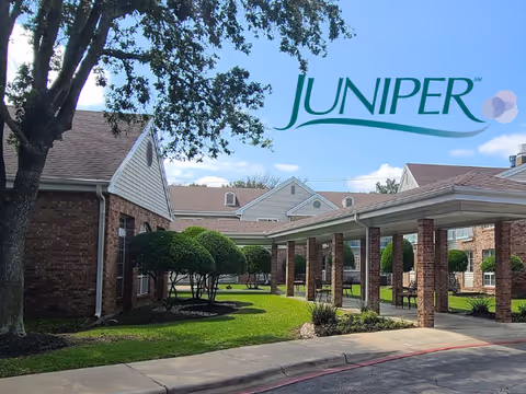 Front exterior of a brick senior living complex with a covered entrance, manicured trees, and a large 'JUNIPER' logo in the sky.