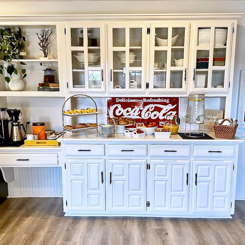 White kitchen cabinets with glass-front doors, Coca-Cola sign, and snack station on counter